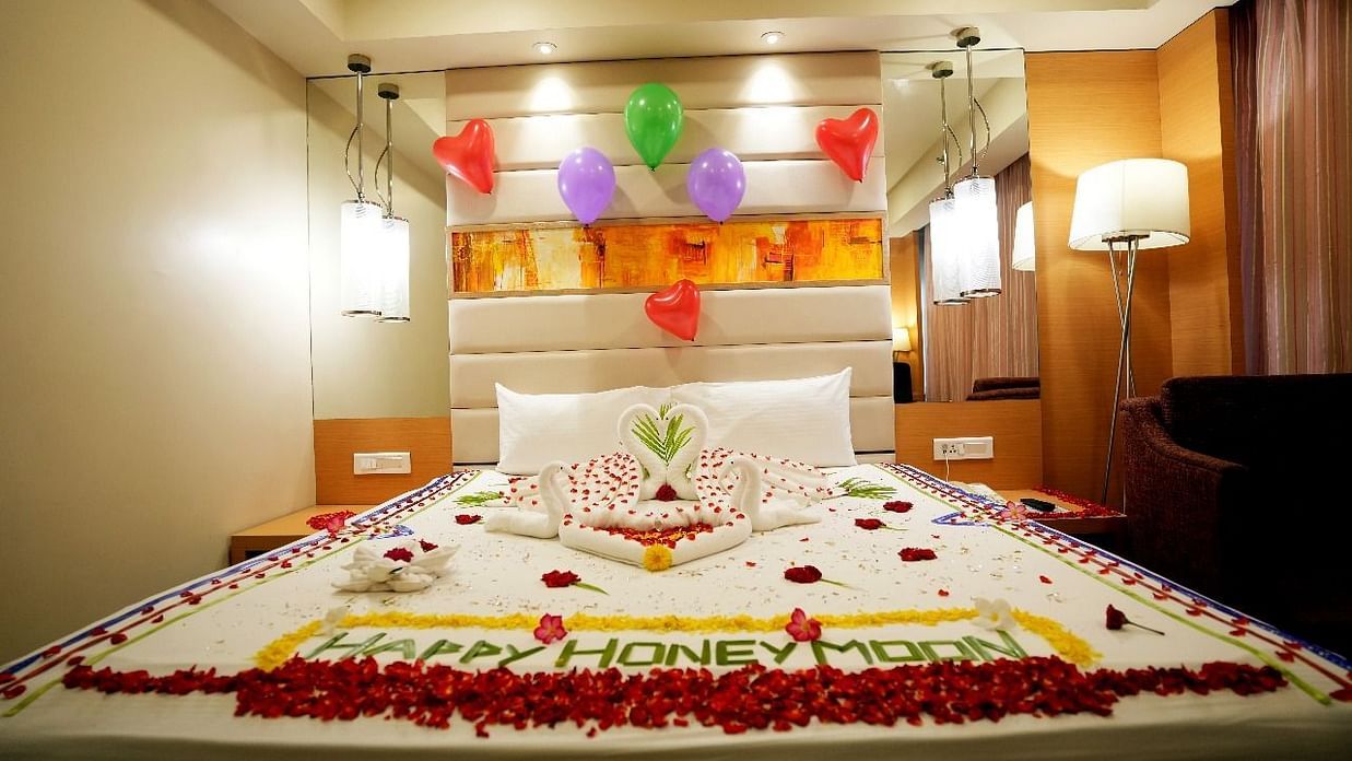 A luxurious hotel room with a beautifully decorated bed adorned with flowers and elegant lighting for Honeymoon