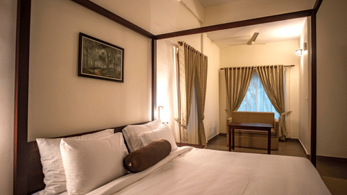 A well-lit bedroom with a traditional wooden bed and soft linens. - Abad Brookside Lakkidi, Wayanad