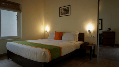 A bedroom is furnished with a neatly made bed, side table, and lamp, offering a comfortable and inviting space. - Abad Brookside Lakkidi, Wayanad