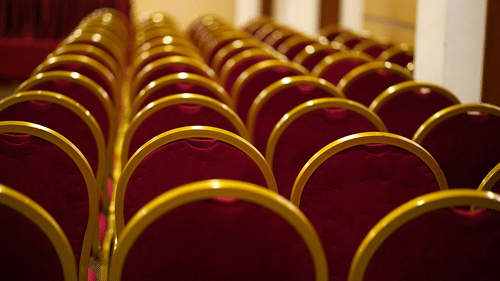 Wide view of empty chairs arranged in neat rows in a large indoor venue, with round, upholstered backs.