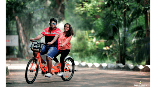 A couple riding a tandem bicycle on a tree-lined path - Black Thunder, Coimbatore