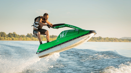 An overview of a person riding a jet ski while standing up on it with waves in view.