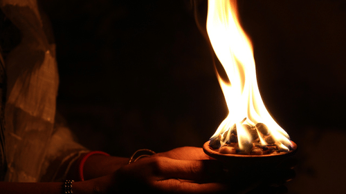 A person holding a flaming diya against a dark background