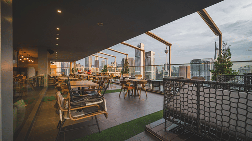 Corner view of a rooftop restaurant with tables and chairs set for diners and view of buildings from there.