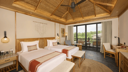Room with a twin beds, ceiling fan, seating area, and balcony access in a wood-themed interior - Royal Tulip, Chitwan