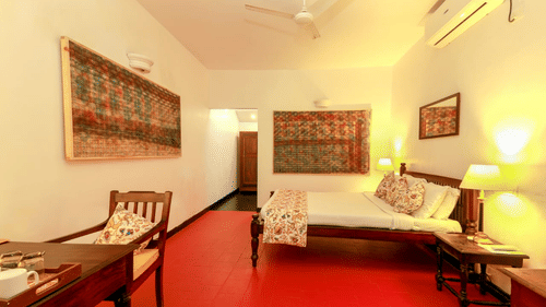 The Tower House - a large king size bed with white linens and bedside lamp along with an air-conditioner. the room also features a workdesk and a balcony facing the garden 