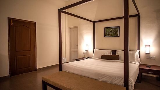 A cosy bedroom with a four-poster bed, warm lighting, and elegant decor. - Abad Brookside Lakkidi, Wayanad