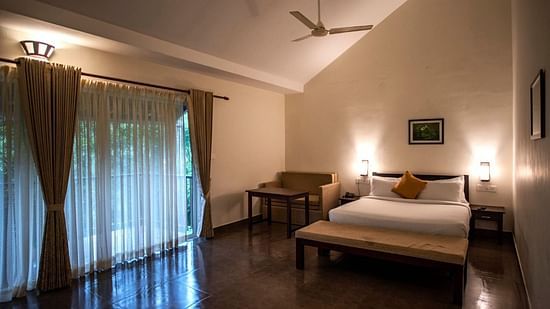 A bedroom with a sofa and sheer curtains offers a comfortable seating area and natural light. - Abad Brookside Lakkidi, Wayanad