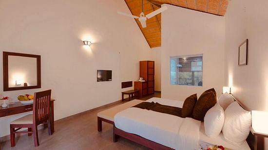 A bedroom with a wooden bed frame features a mirror and a side table, creating a comfortable interior. - Abad Brookside Lakkidi, Wayanad