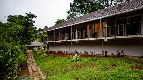 A long building with a balcony overlooks a well-maintained garden, offering a scenic view. - Abad Brookside Lakkidi, Wayanad