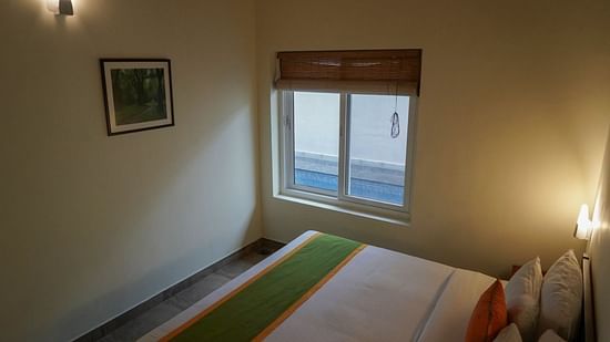 A view of a bedroom shows a window, providing natural light and a view of the surroundings. - Abad Brookside Lakkidi, Wayanad