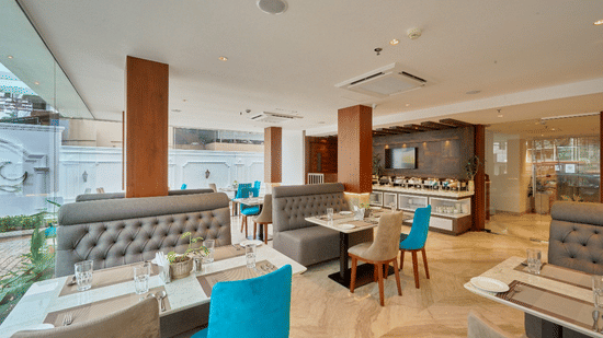 Wide view of the restaurant at QWhite Crescent Luxury Hotel by Dimora Kochi with teal chairs, cushioned booths, and warm ambient lighting.