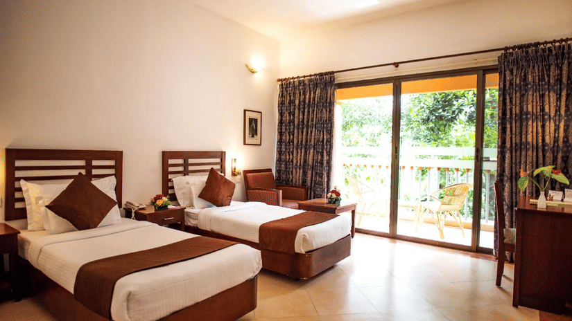 Bright bedroom at Abad Green Forest with twin beds, balcony views, and nature-inspired comfort near cottages in Thekkady.