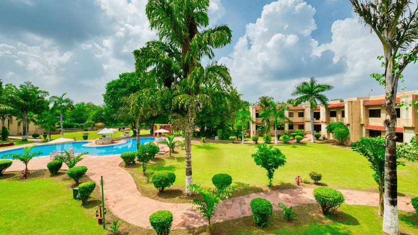 Landscaped garden with walking paths, palm trees, outdoor pool and resort buildings at Clarks Khajuraho.