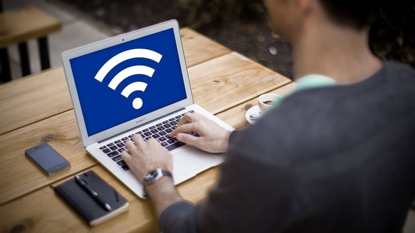 A man sits outdoors, working on a laptop with a prominent Wi-Fi symbol on the screen.