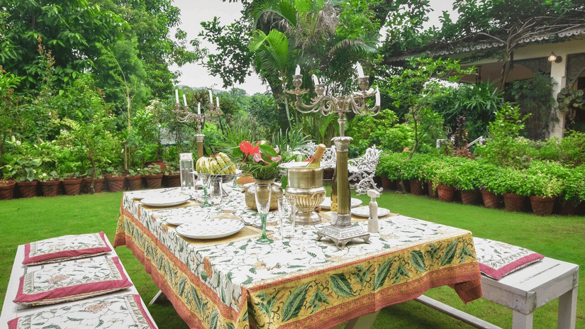 Dining arrangement in the lawn at Shaheen Bagh, in Dehradun featuring tables and stools with cutlery and candles set on the table surrounded by greenery