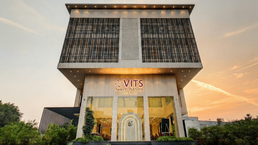 Facade of VITS Select Nashik Hotels & Resorts under a vibrant sky with the well-lit exteriors surrounded by bushes