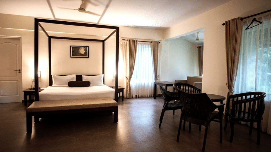 A well-lit bedroom with a four-poster bed, wooden furniture, and large windows.- Abad Brookside Lakkidi, Wayanad