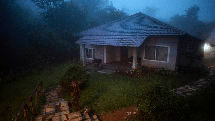 A misty evening scene featuring a cosy house with a tiled roof and a garden.- Abad Brookside Lakkidi, Wayanad