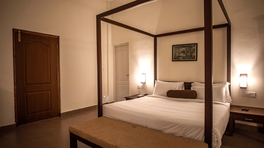 A modern bedroom with a four-poster bed, seating area, and large windows.- Abad Brookside Lakkidi, Wayanad