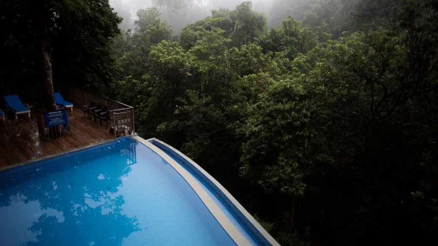 A mist-covered pool with blue water is nestled among green trees.- Abad Brookside Lakkidi, Wayanad