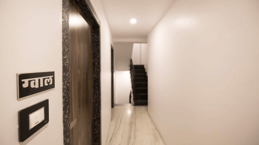 hallway of Adamo Sanmukh next to a room door with a gwal nameplate next to it.