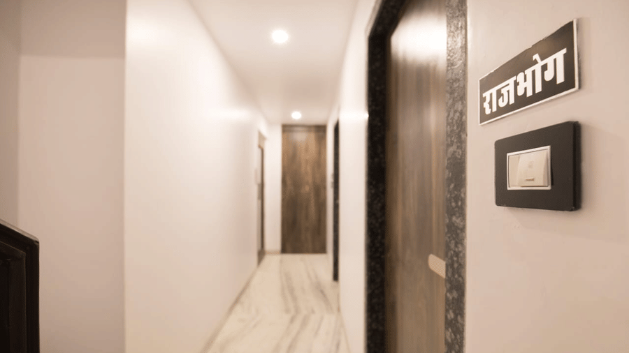 Hallway of Adamo Sanmukh with a room door and a rajbhog namplate next to it.