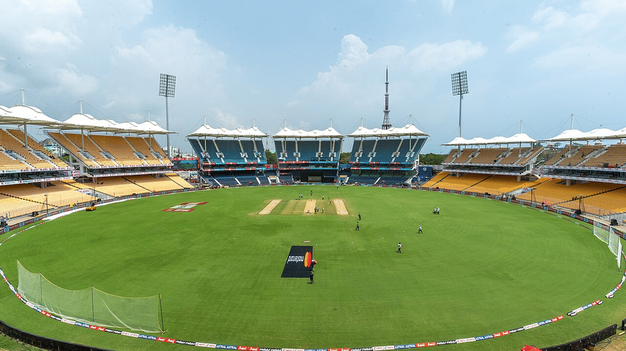 Modern bowl-shaped cricket stadium with lush central square, sight screens, and yellow seating curving around the field.