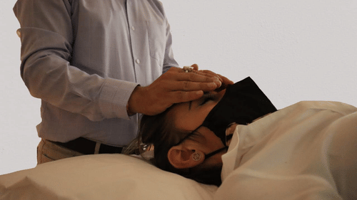 A man gently placing his palm on a person s forehead as they close their eyes at YO1 Longevity and Health Resorts