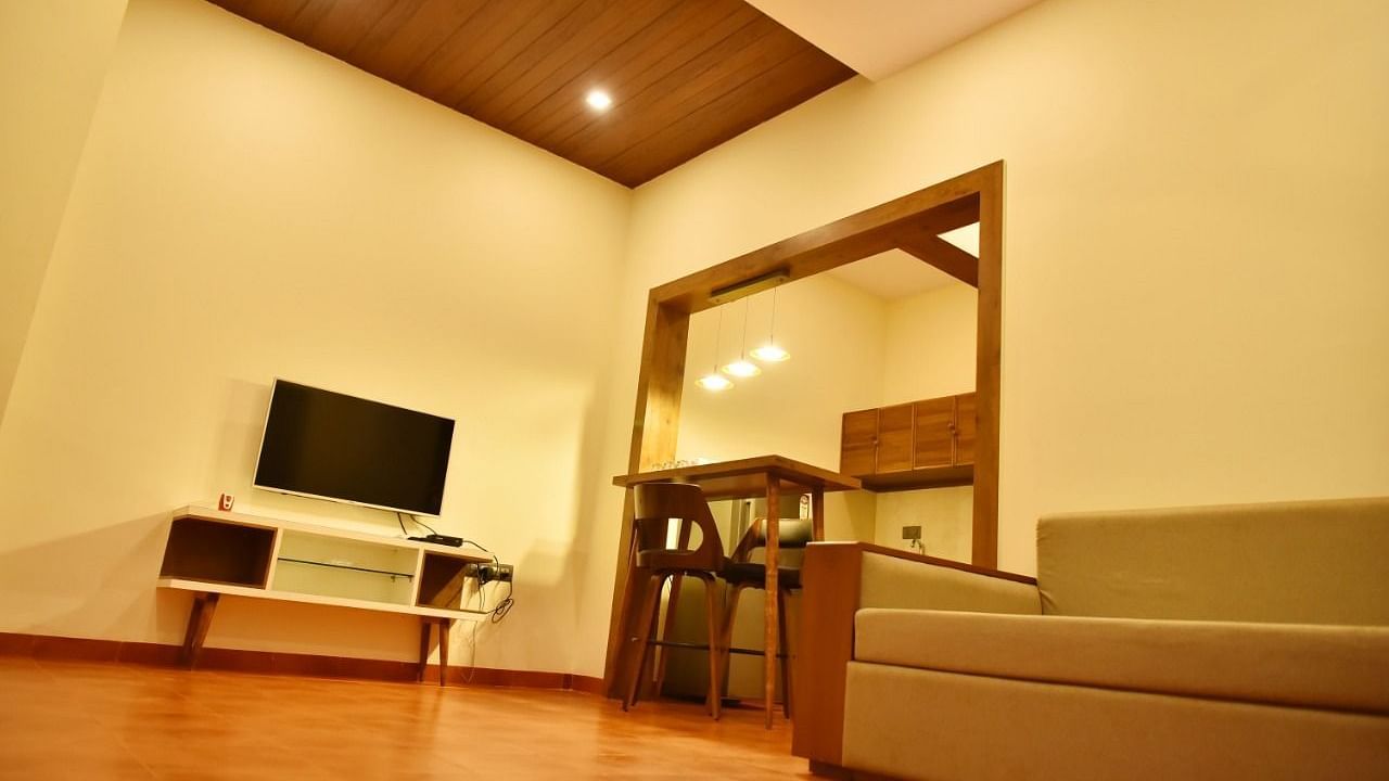  Modern living area with a dark wood panelled ceiling, TV, and a glimpse of a kitchen.