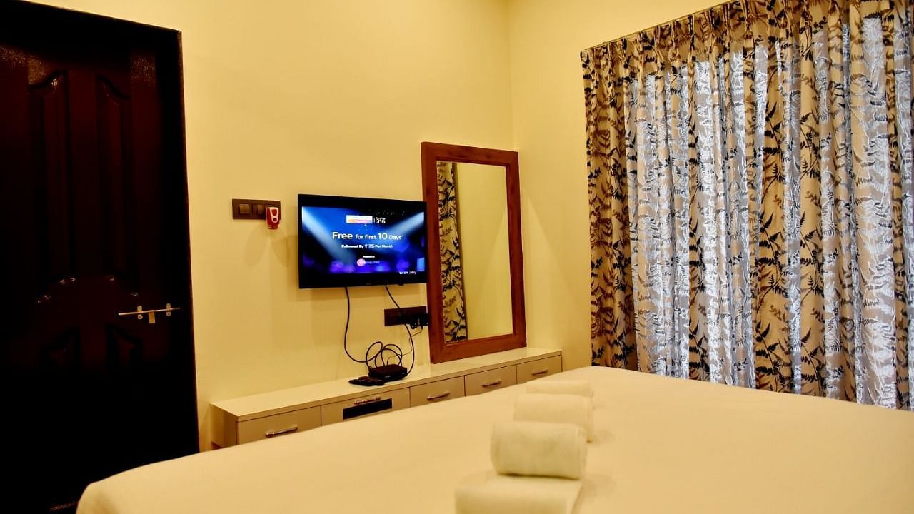 A simply furnished bedroom with a bed, TV, dresser, mirror, and beige walls.
