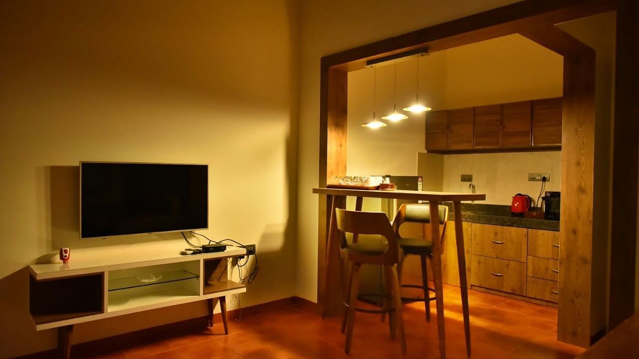 Warmly lit living space with a TV unit, high-top dining table, and an open kitchen featuring wooden cabinets.