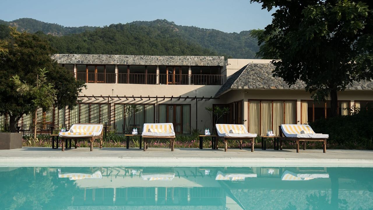 The outdoor swimming pool at Saraca Resort & Spa Corbett with lounging chairs placed in the backdrop
