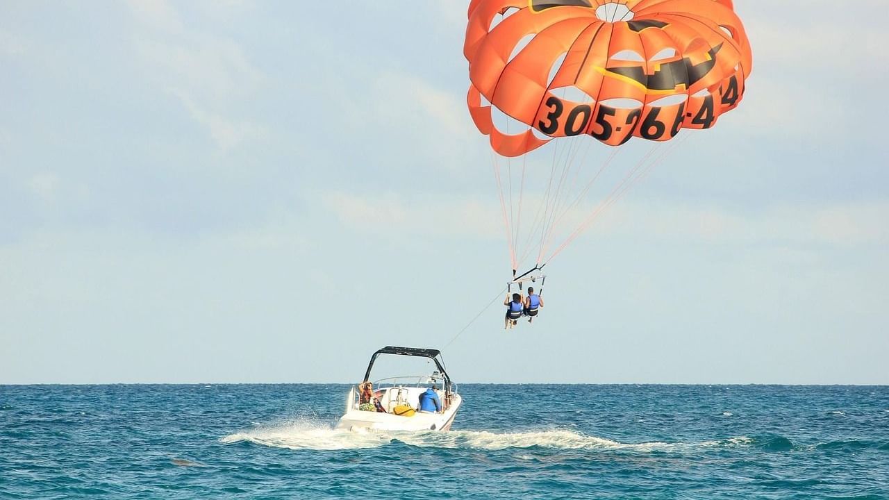 A boat sailing in the ocean with a person parasailing featuring an orange coloured parachute.