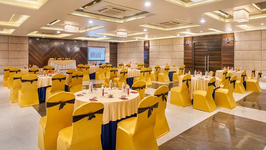 A spacious event hall at Lords Inn Porbandar, is prepared with round tables and chairs with yellow sashes, ready for guests.