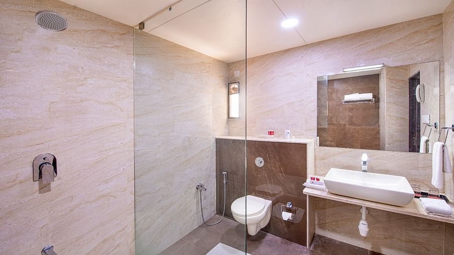 A bright and modern hotel bathroom is equipped with a glass-enclosed walk-in shower, a sleek countertop washbasin, and a toilet.