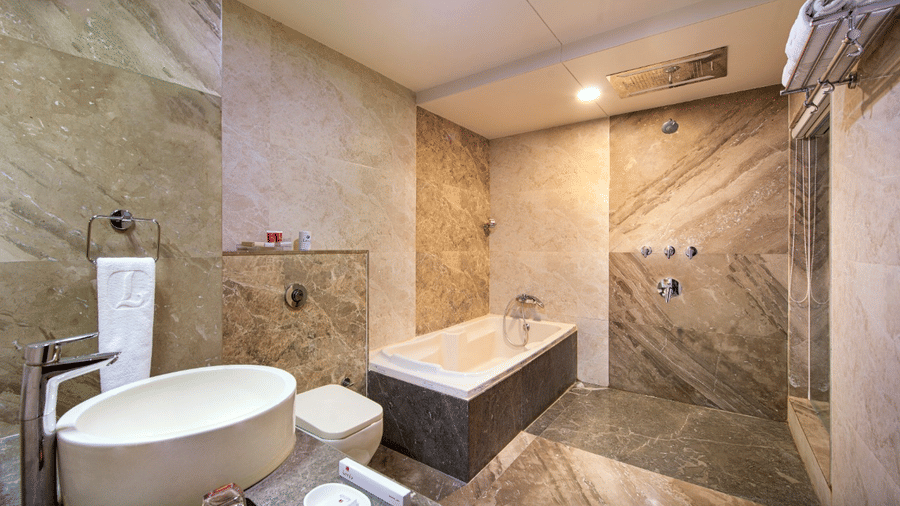A clean and modern hotel bathroom includes a soaking bathtub, a contemporary washbasin, and tiled walls with shower fixtures.