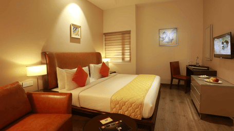 An Executive Room at The Mayberry, Tiruppur, with a bed, a wall-mounted TV, a table with a chair, and a sofa.
