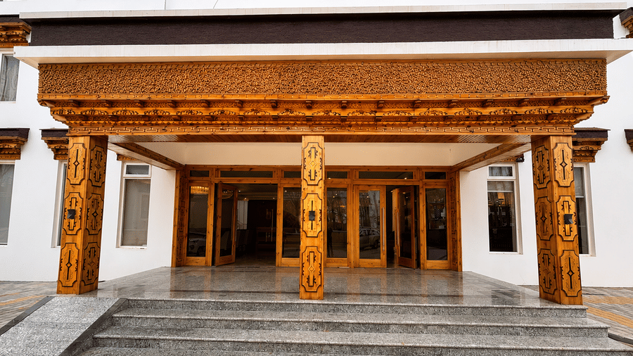 Hotel entrance with carved wooden pillars and beams in a traditional style, glass doors and a paved courtyard leading up to the building.