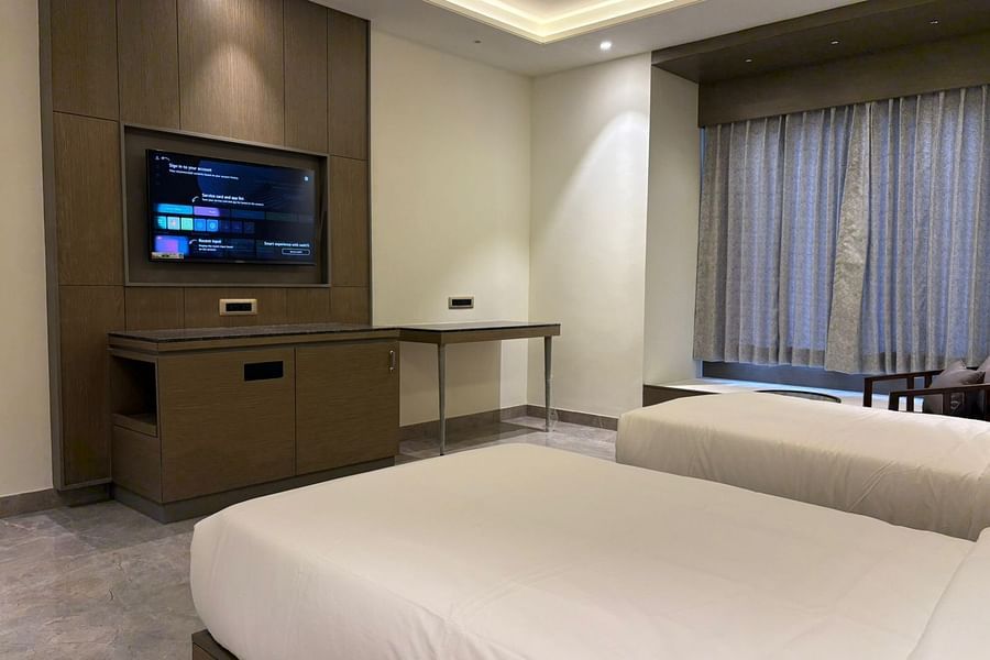 An image of a bedroom featuring twin beds and a flat TV screen - Pride Hotels Group