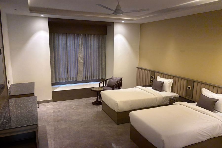 An image of a bedroom featuring twin beds and a chair paired with centre table at Pride Hotels Group