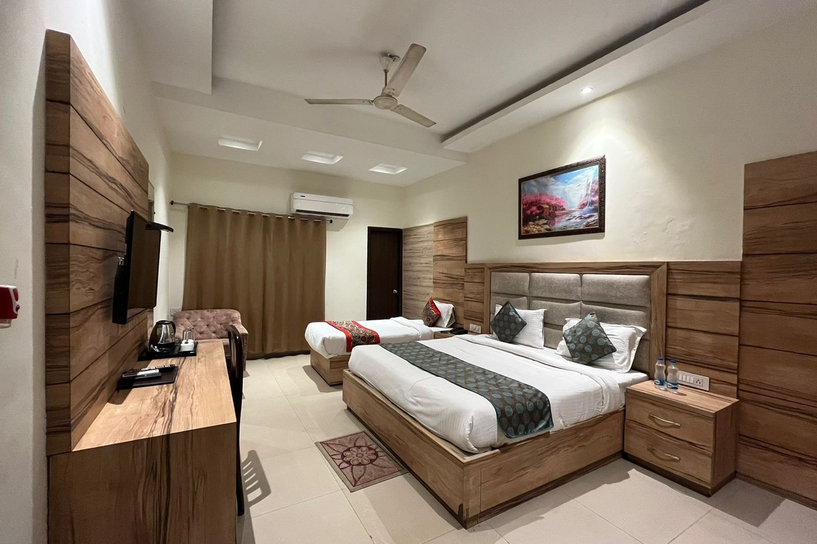 A clean, modern hotel room with a single queen-sized bed, a wooden headboard, and a flatscreen TV mounted on the wall.
