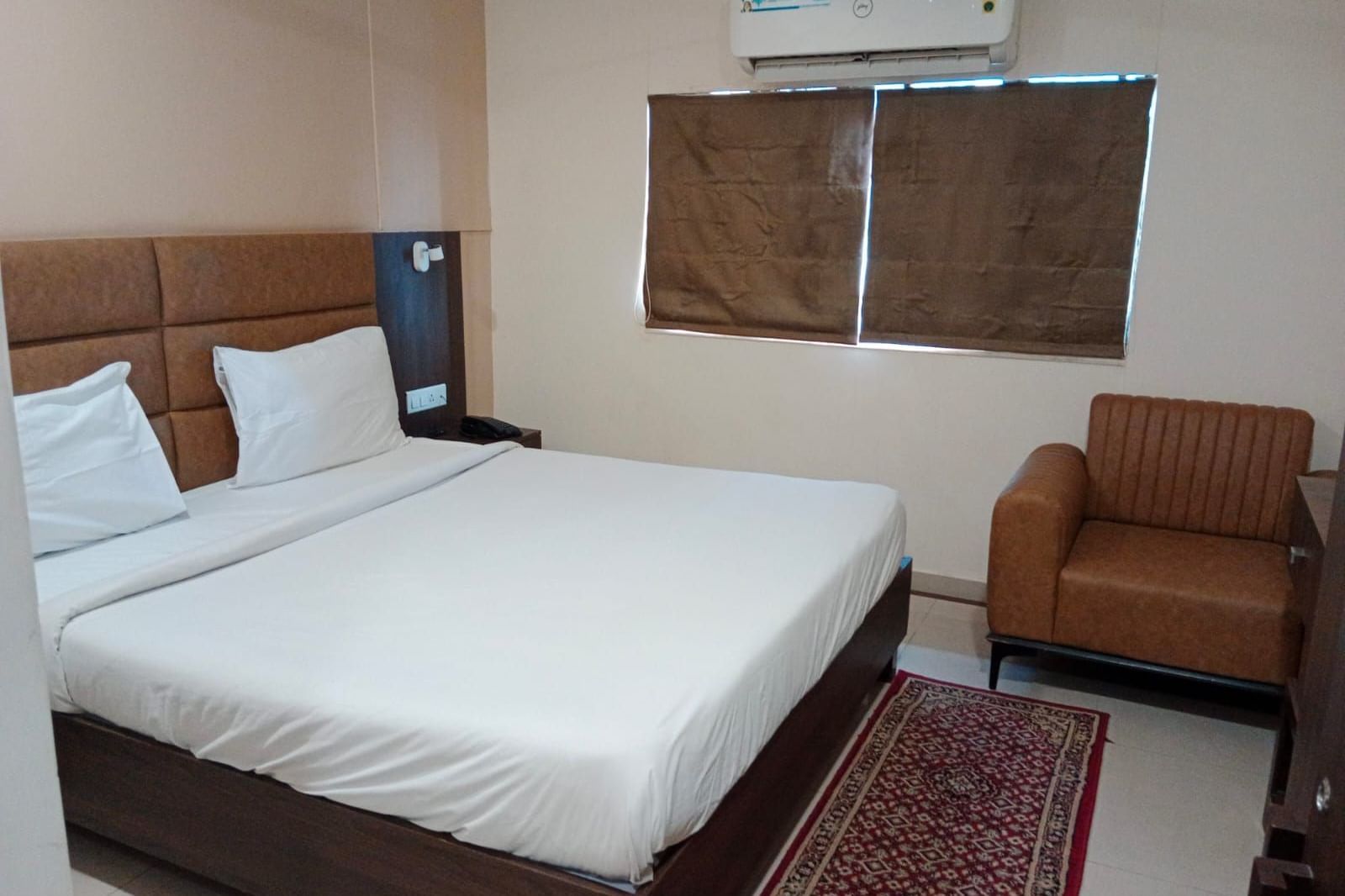 Side view of a double bed at Pravasa Ahmedabad with a brown leather armchair in the corner.
