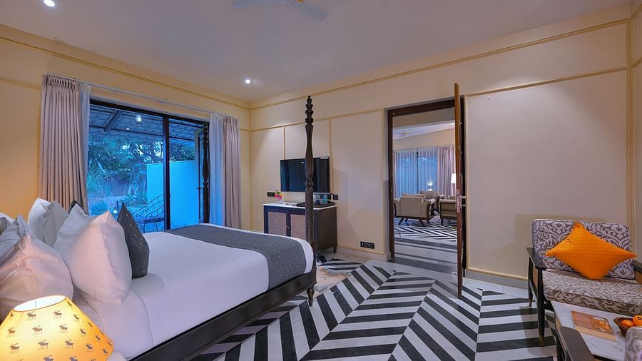 Luxury Suite Cottage with a four-poster bed, black and white chevron flooring, a seating area with an orange pillow, and a view into a living area - Singhvilas, Ranthambore
