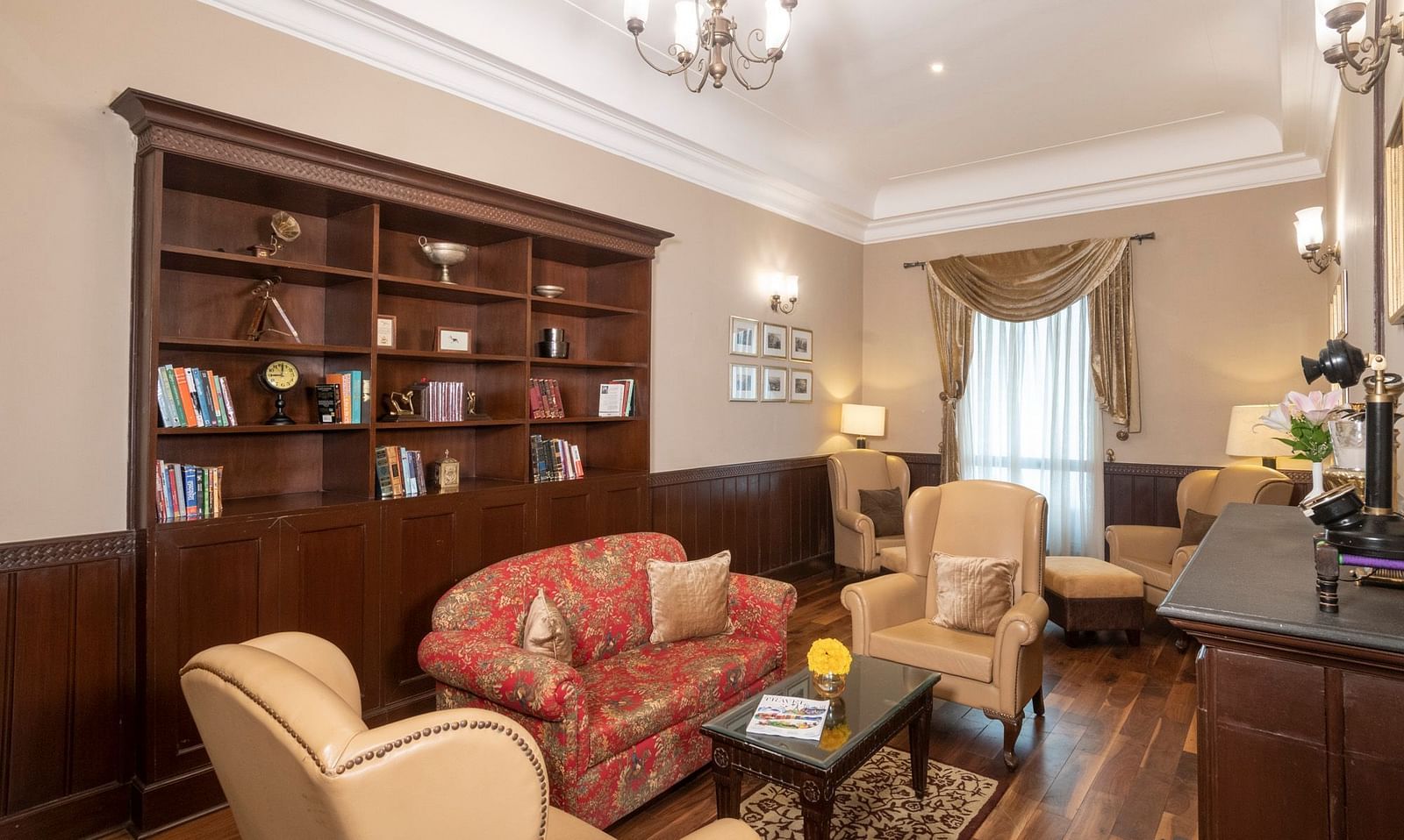 The Library is furnished with classic vintage sofa, two armchairs, a coffee table, a wooden cupboard displaying books, and a window