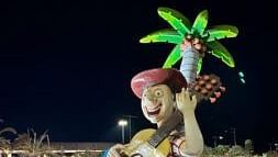 The night view of the a boy big statue playing guitar surrounded by big palm tree and lights