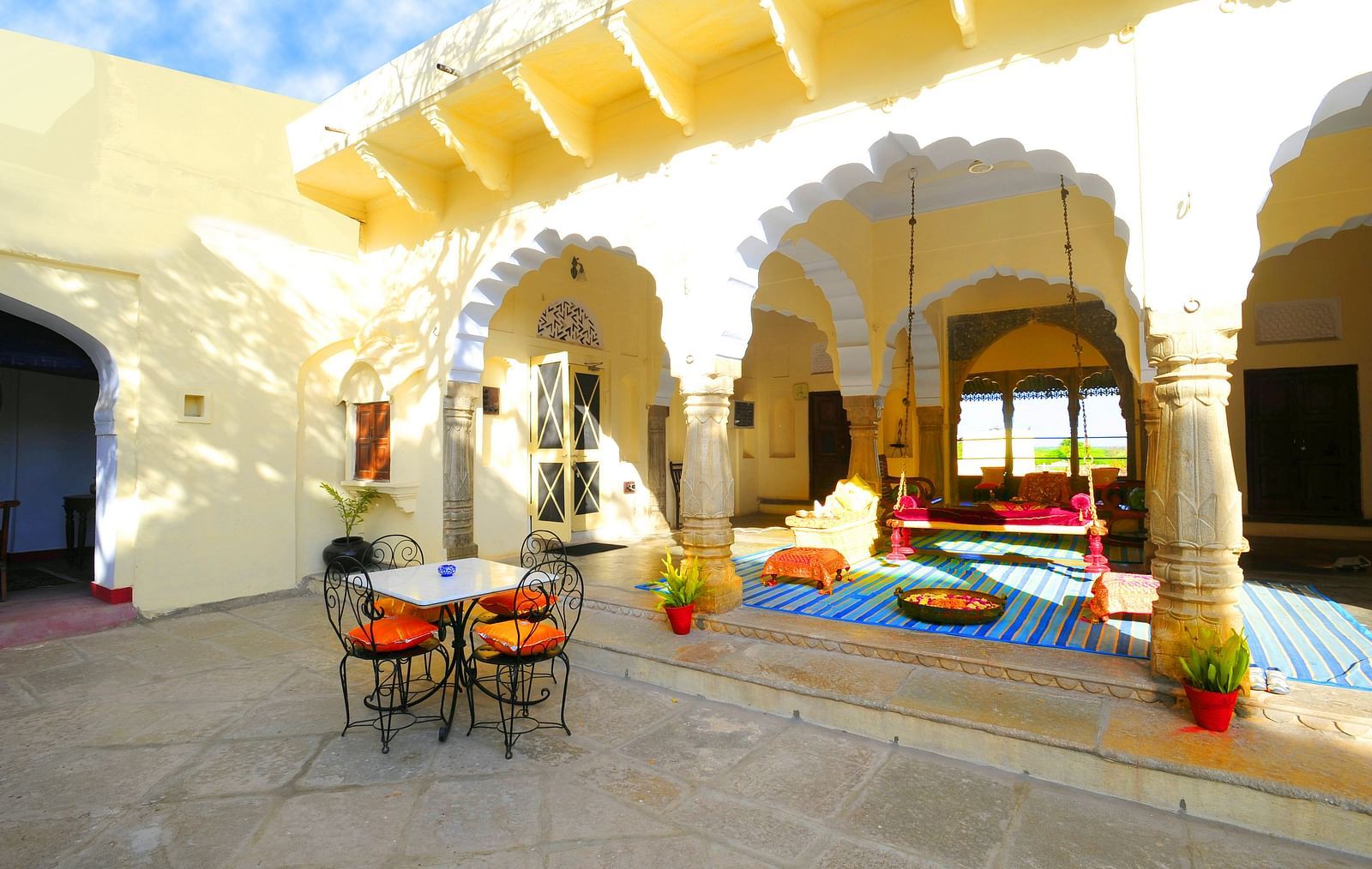 A sun-drenched courtyard at Fort Barli, with arched colonnades and a swing, offers a charming blend of architecture and relaxation.