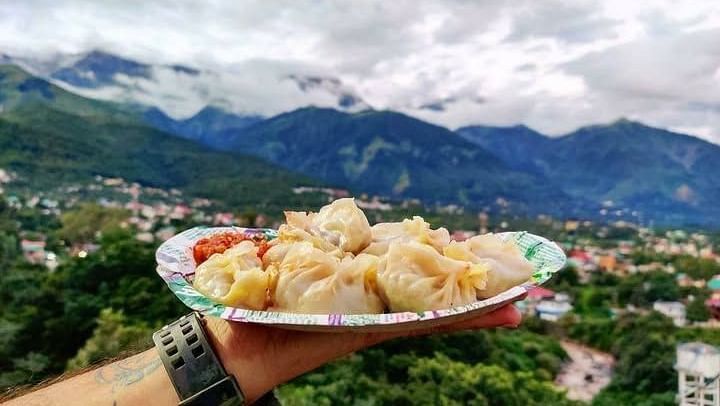A man holding a plate of momo with hills on the background.