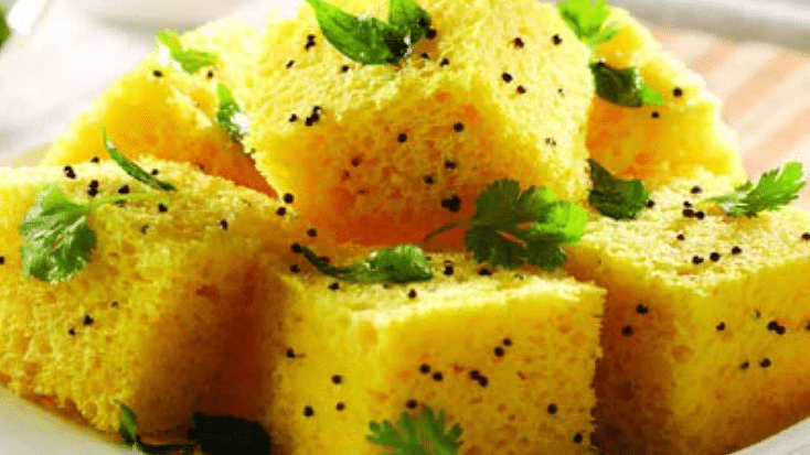 A close-up view of fluffy khaman served on a plate, beautifully garnished with mustard seeds and fresh coriander leaves.