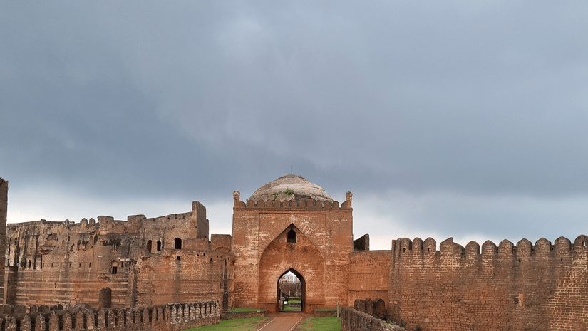 Exterior view of a historic red fort with stone walls and arched entrance.